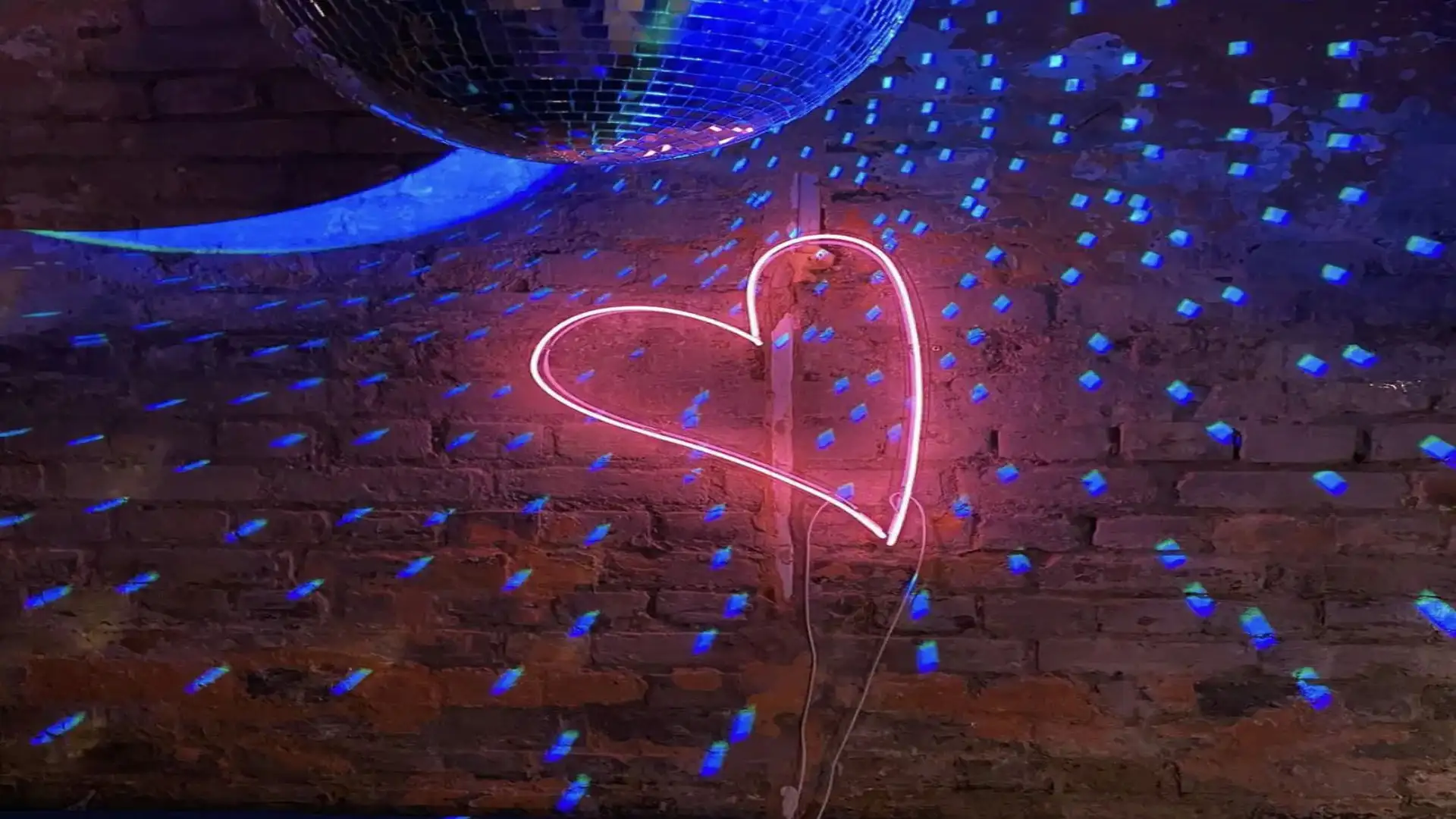 A pink neon heart on an exposed brick wall next to a disco ball