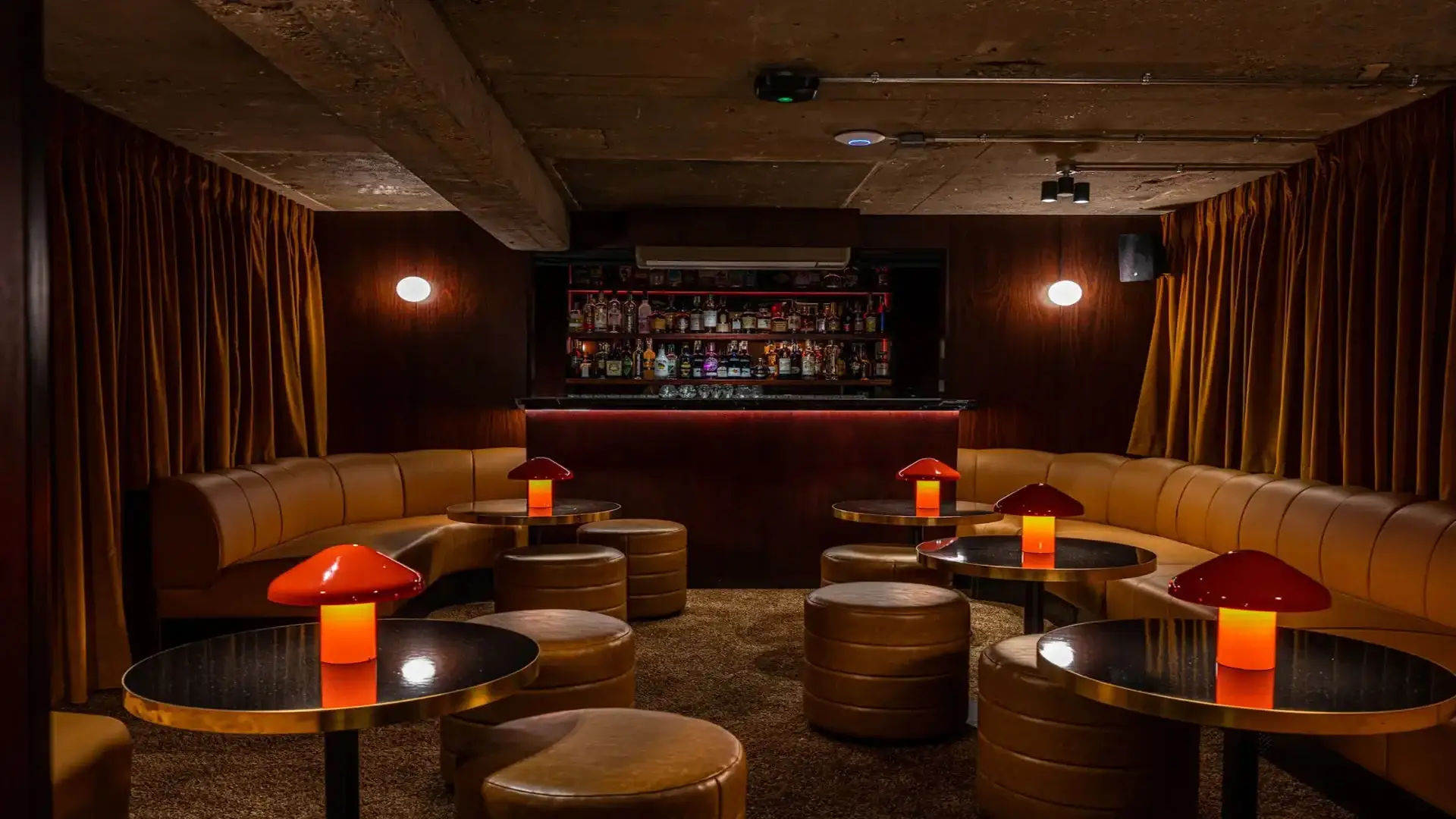 Discreet, members club style cocktail bar in rich mahogany with lava red lamps and leather seating