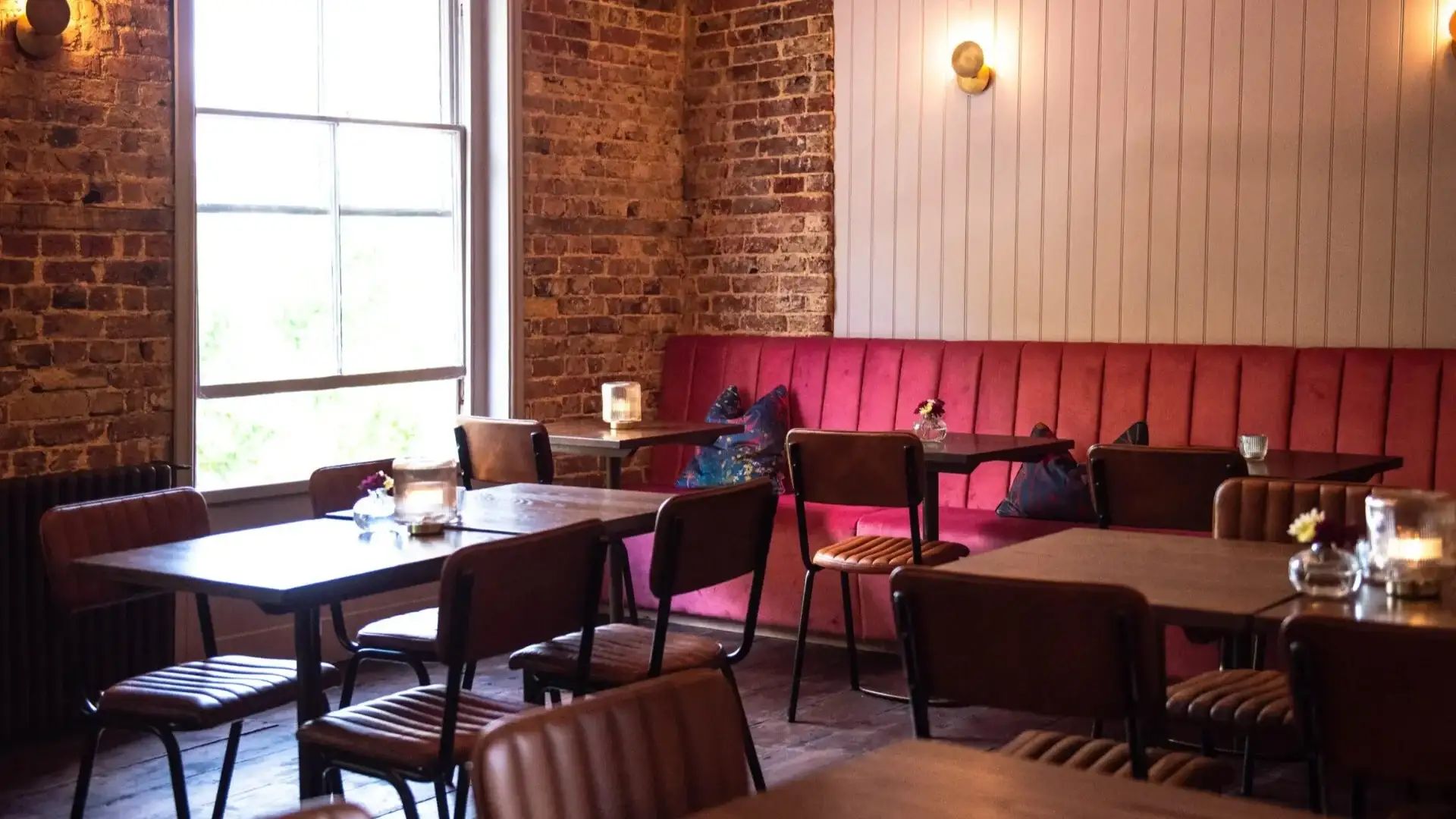 Red banquettes line the room with exposed brick walls, funky cushions and plenty of natural light